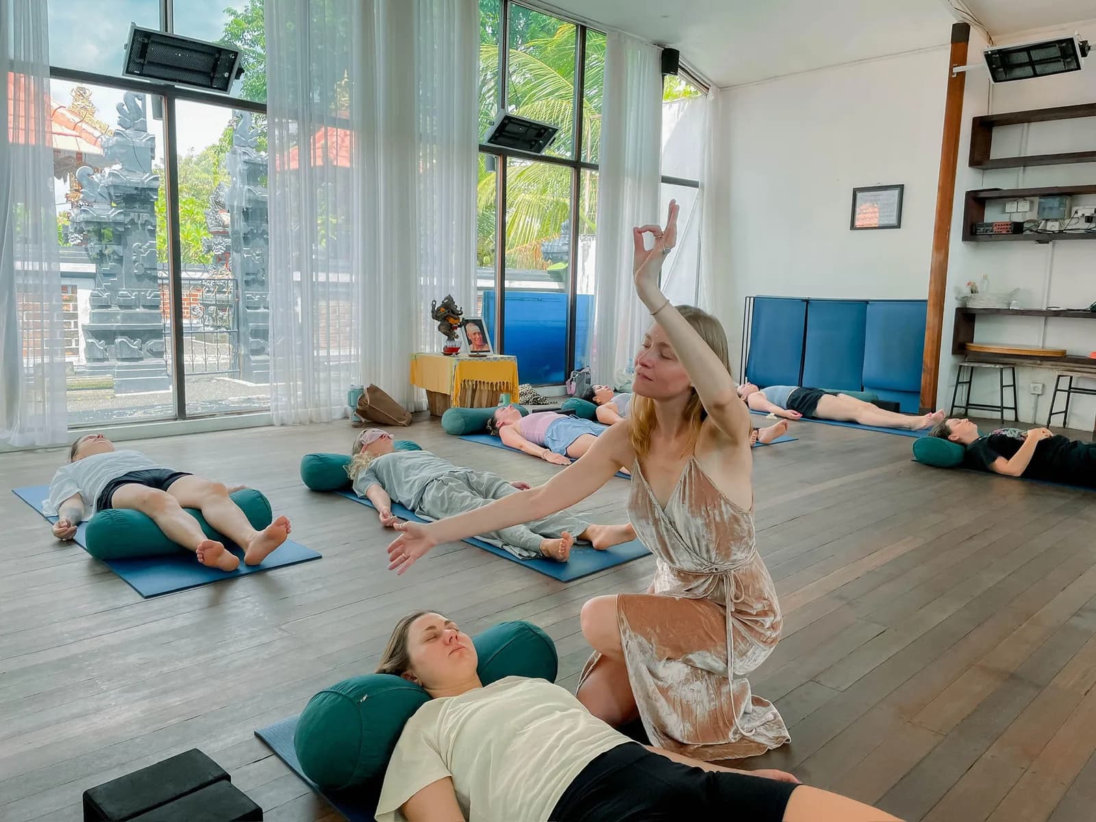 Alina leading a group session in a Bali studio, participants lying on mats around her