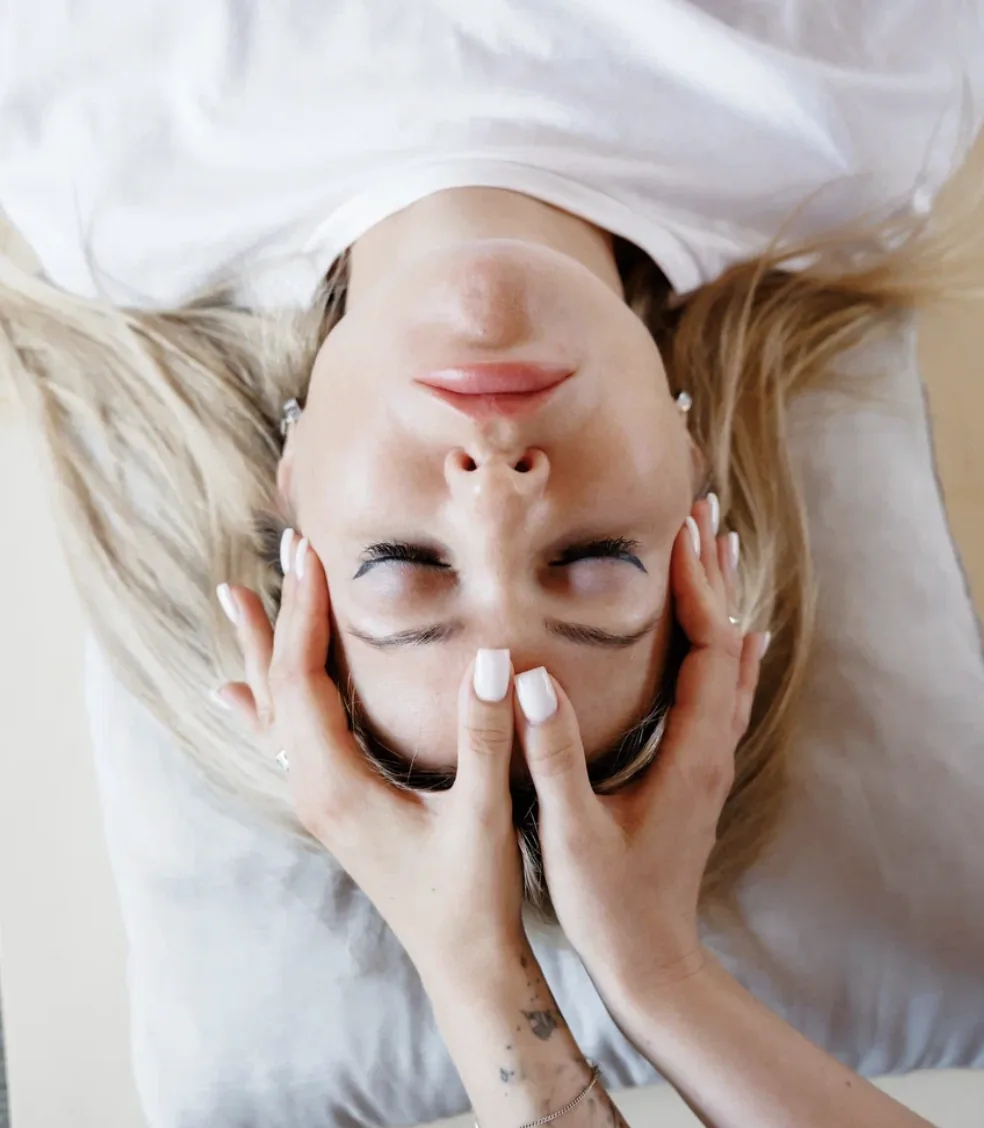 A woman lying down with her eyes closed and her hands resting on her face