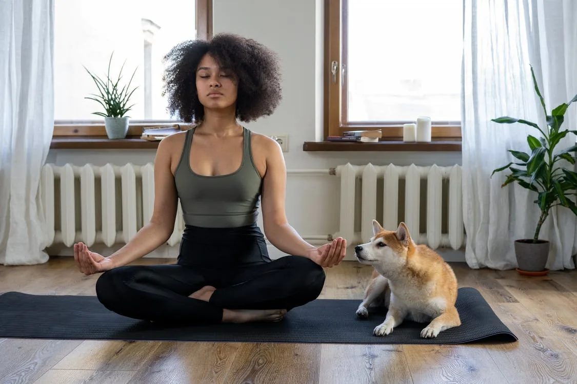 A curly girl meditating in lotus pose with a c ute dog next to her | meditation is for each and every one
