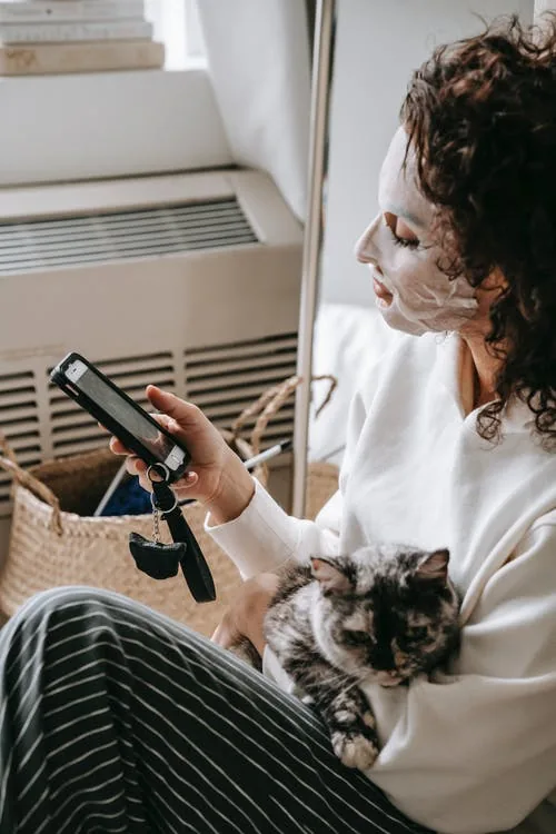 woman scrolling on her phone with face mask on and cat in her hands, screen time managing